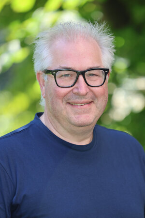 Portraitfoto Axel Kelm in Zivilkleidung vor einer grünen Buchenehecke