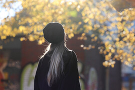 Symbolbild: Eine junge Frau atmet unter einem Baum mit goldenem Herbstlaub bei Sonnenschein tief ein