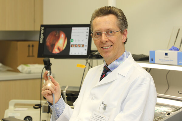 Prof. Dr. Andreas Naumann im weißen Kittel mit einem Endoskop und entsprehendem Monitor im Hintergrund