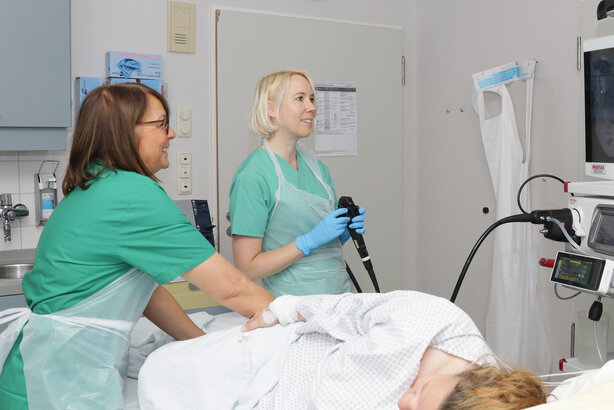 Zwei Mitarbeiterinnen beobachten auf einem Monitor eine Bronchoskopie - der Patient liegt im Vordergrung