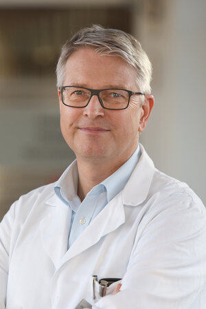 Portraitfoto Dr. Andreas Kastrup im blauem Hemd und Arztkittel