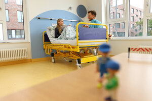 Ein Kinderkrankenzimmer mit Arzt auf der Bettkante eines kranken Mädchens