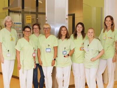 Gruppenfoto: 8 junge Frauen in grünen Kasacks vor dem Ambulanztresen