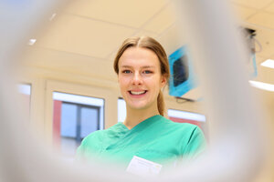 Pflegekraft in grüner Dienstkleidung vor einem Deckenmonitor