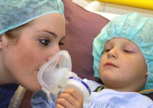Pflegekraft mit OP-Haube bekommt von einem Kind eine Sauerstoffmaske aufgesetzt - OP-Vorbereitung
