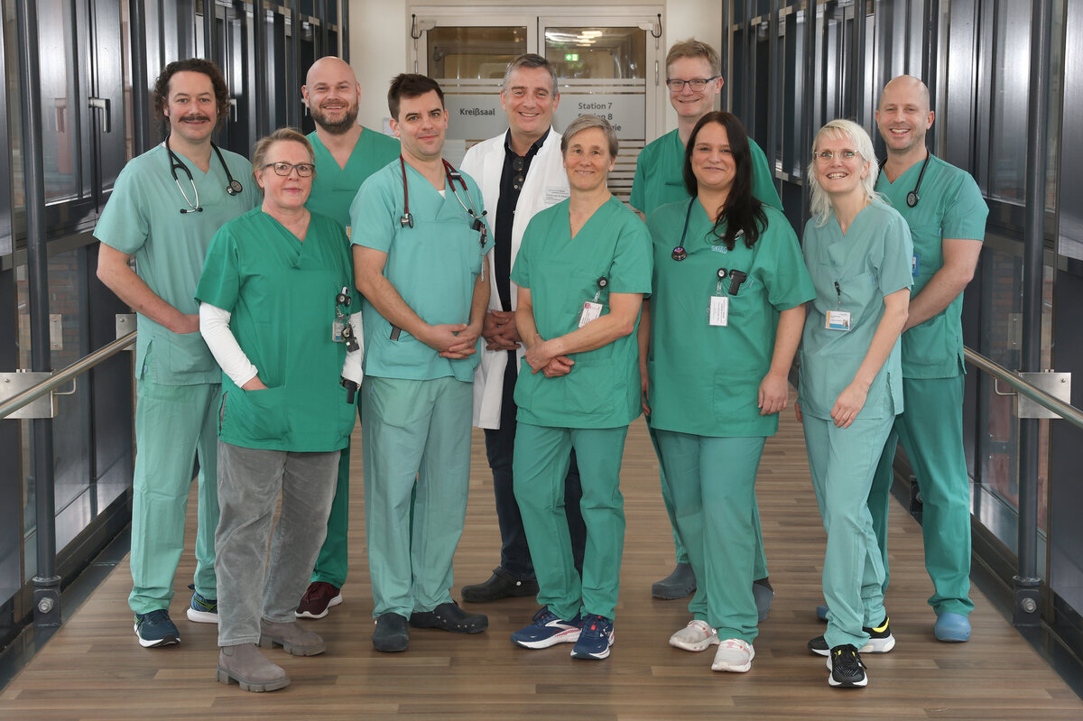 Zehn Oberärztinnen und Oberärzte in grüner Funktionskleidung als Gruppenbild auf einem Verbindungsgang im Krankenhaus